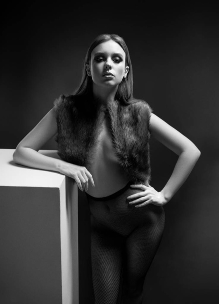 Half body view of woman in fur waistcoat and tights posing on dark background - Photo, Image