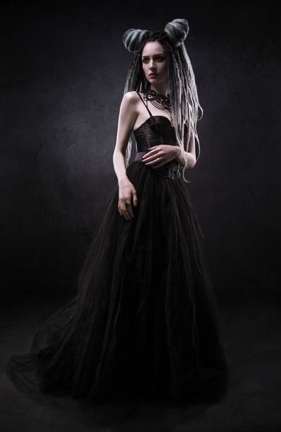 Woman with dreads and black gothic dress posing on dark background - Фото, зображення
