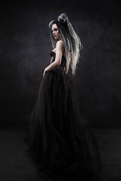 Woman with dreads and black gothic dress posing on dark background - Photo, Image