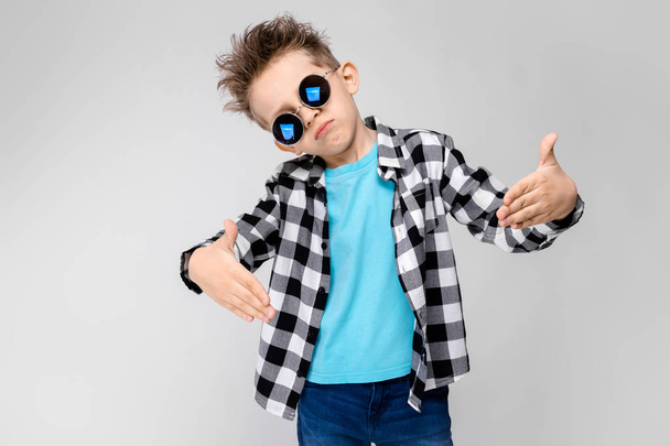 Niño caucásico en traje casual y gafas de sol redondas que muestran diferentes expresiones en la pared blanca en el estudio
. - Foto, Imagen