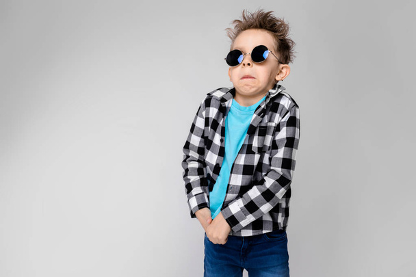 Niño caucásico en traje casual y gafas de sol redondas que muestran diferentes expresiones en la pared blanca en el estudio
. - Foto, Imagen