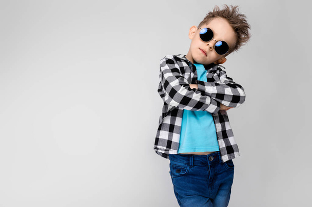 Niño caucásico en traje casual y gafas de sol redondas que muestran diferentes expresiones en la pared blanca en el estudio
. - Foto, imagen