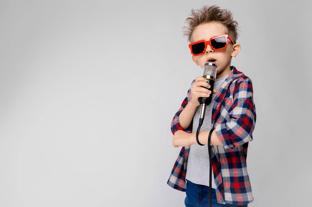 Nizza bambino caucasico prescolare in abito casual posa in occhiali da sole partito con microfono e mostrando diverse espressioni sulla parete bianca in studio
. - Foto, immagini