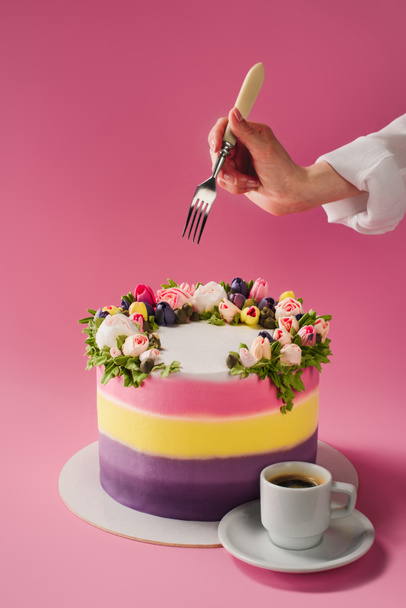 cropped shot of woman with fork, cup of coffee and cake decorated with cream flowers isolated on pink - Foto, Imagen