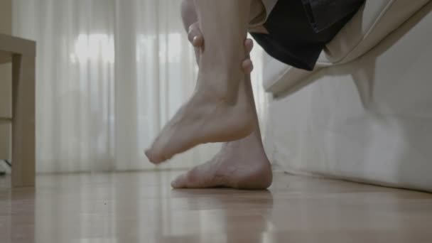 Patient mature man with arthritis sitting on bed and rubbing his ankle and foot relieving the ache - Filmmaterial, Video