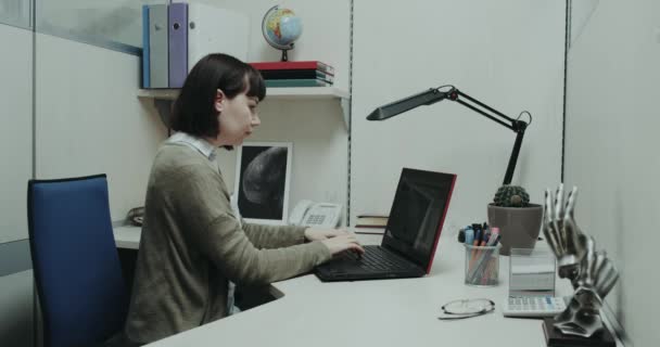Young women in office sitting at her desk tapping on keyboard in notebook. red epic - Záběry, video