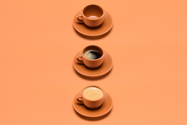close up view of arrangement of empty cup and two cups of coffee isolated on peach - Foto, immagini