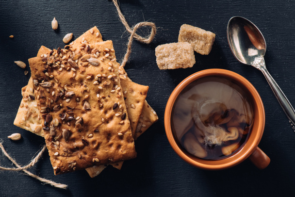 vista superior de las galletas, taza de café, cuchara y azúcar morena en la mesa oscura
 - Foto, Imagen