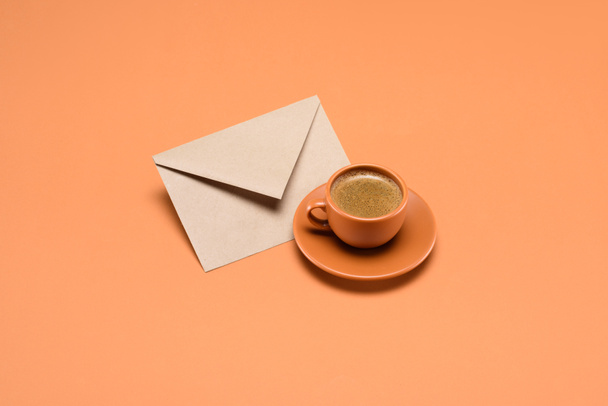 close up view of cup of coffee on saucer and envelope isolated on peach - Fotó, kép