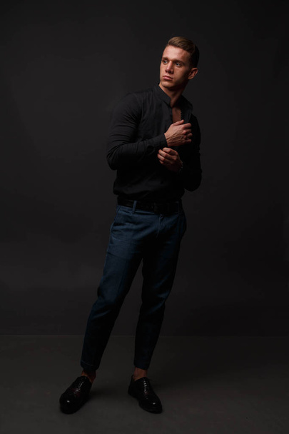 attractive white man in black shirt and blue pants stands on a dark background - Foto, immagini
