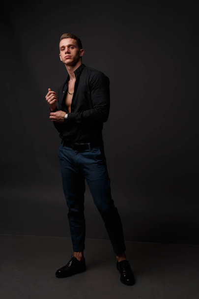 attractive white man in black shirt and blue pants stands on a dark background - Фото, зображення