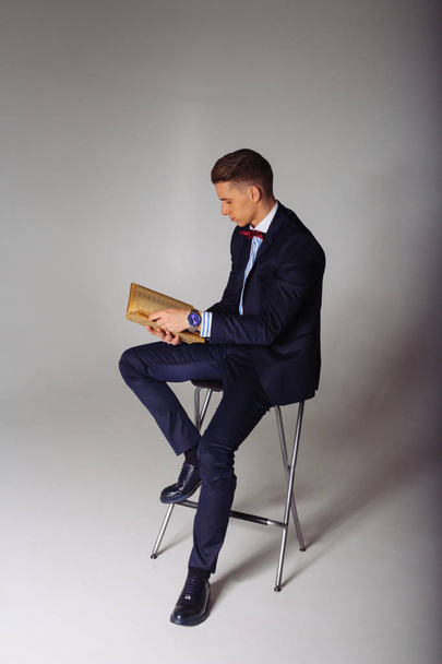 a man, a guy in a blue suit, sits on a chair and reads an old book, the concept of knowledge, study, science, business, everything new, its a well-forgotten old - Foto, Bild