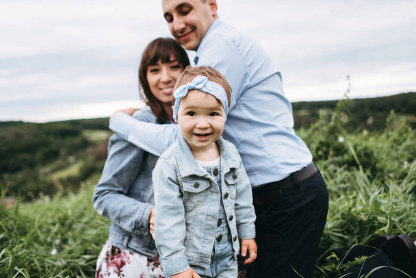 View of woman sitting on grass with man and little girl smiling and standing ahead - Photo, Image