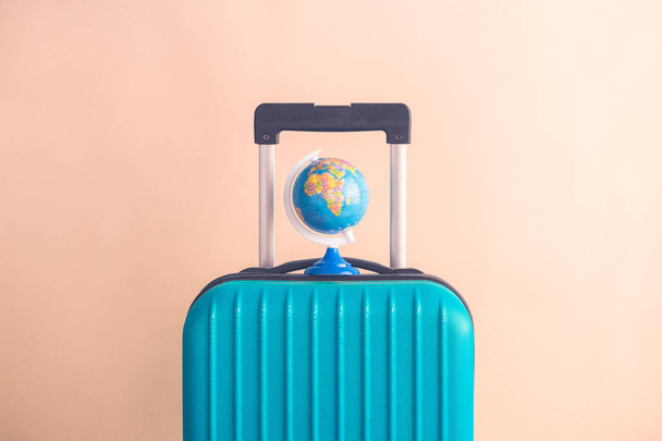 Luggage with small globe on beige background minimalistic vacation concept - Photo, Image