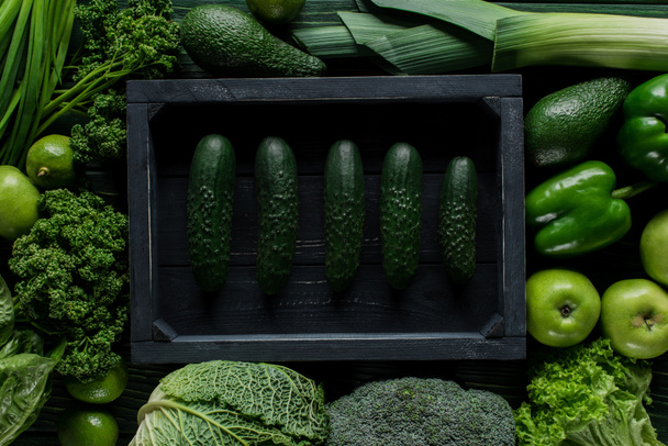 top view of cucumbers in wooden box between green vegetables, healthy eating concept - Photo, Image