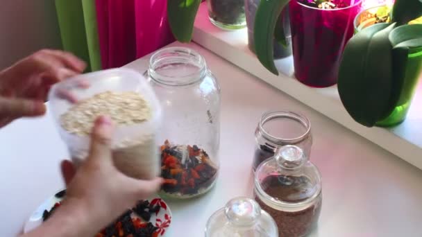 The man mixes in a glass jar a dried fruit, oat flakes to get muesli. - Séquence, vidéo