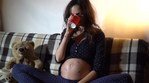 Счастливая беременная женщина отдыхает на диване и гладит животик.
. - Кадры, видео