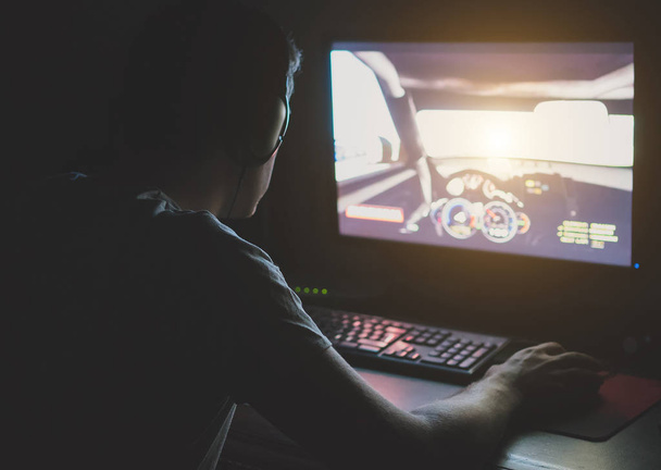 Man in headphones playing computer car racing game at night. - Foto, afbeelding