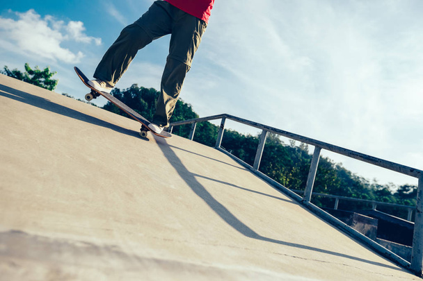 Skateboarder legs riding skateboard on skatepark ramp - Fotó, kép