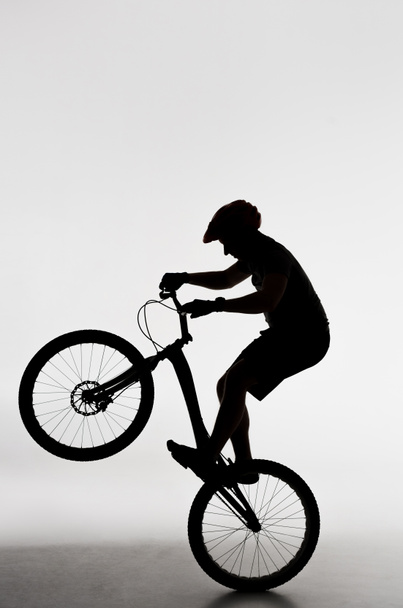 silueta del motociclista de prueba de pie en la rueda trasera en blanco
 - Foto, Imagen
