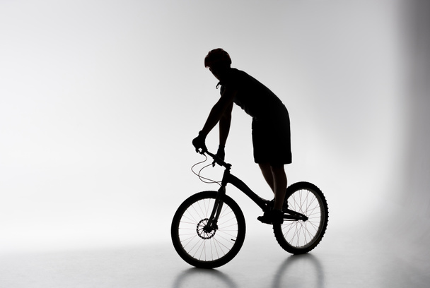 silueta del ciclista de trial en casco equilibrado en bicicleta en blanco
 - Foto, imagen