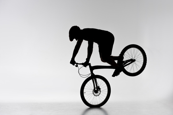 silhouette of trial cyclist performing front wheel stand on white - Photo, Image