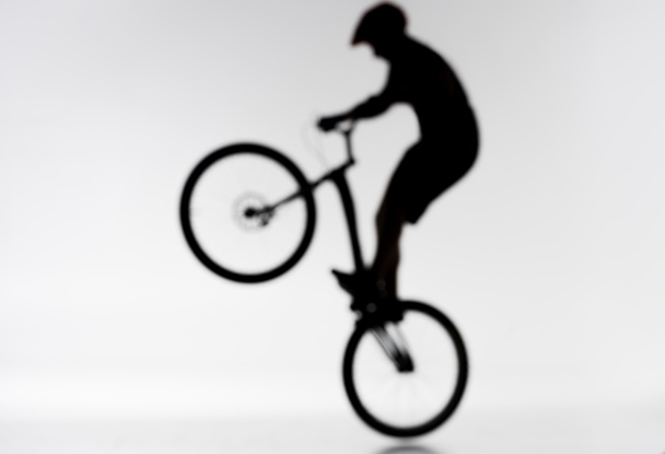 borrosa toma de silueta de trial motorista realizar conejito hop en blanco
 - Foto, imagen