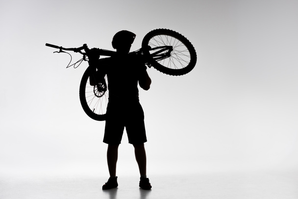 sziluettjét próba-motoros kerékpár vállán tartja a fehér - Fotó, kép
