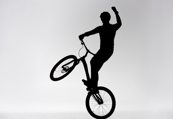 silhouette di trial biker in piedi sulla ruota posteriore e alzando la mano sul bianco
 - Foto, immagini