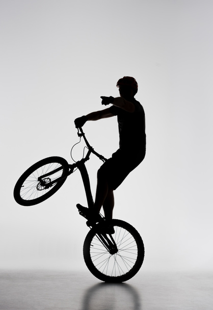 silueta del motociclista de prueba de pie en la rueda trasera y apuntando en algún lugar en blanco
 - Foto, imagen