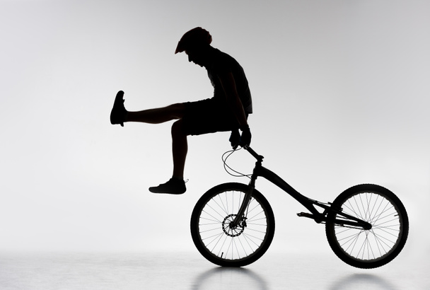 silhouette of trial cyclist standing on handlebars with hands on white - Photo, Image