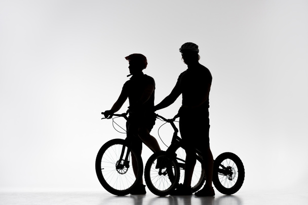 silhouettes of trial bikers in helmets with bicycles on white - Photo, Image