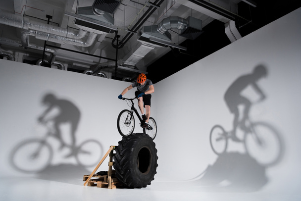 молодий спортивний пробний велосипедист балансує на тракторному колесі
 - Фото, зображення