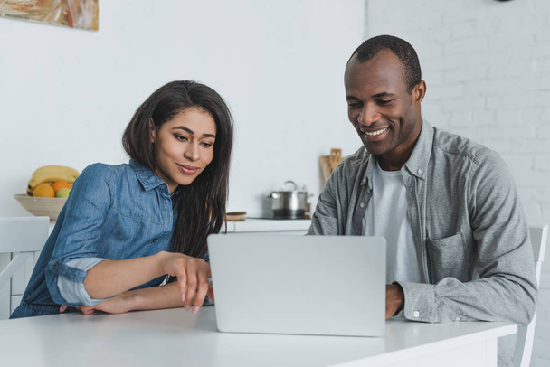 happy african american girlfriend and boyfriend looking at laptop at home - Фото, изображение