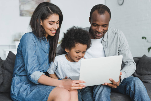 african american parents and son holding laptop and sitting on sofa at home - Photo, image