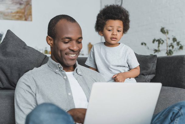 african american son watching how father using laptop at home - Fotografie, Obrázek