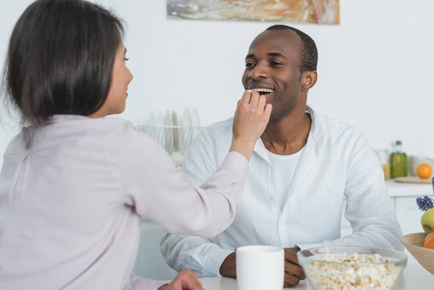afro-americano namorada alimentando namorado com pipocas em casa
 - Foto, Imagem