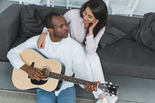 hoge hoekmening van Afro-Amerikaanse vriend gitaarspelen voor vriendin thuis - Foto, afbeelding