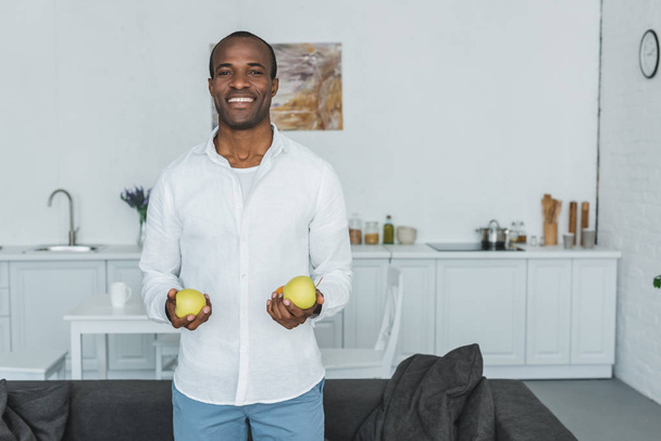 usmívající se pohledný americký muž, který držel jablka doma - Fotografie, Obrázek