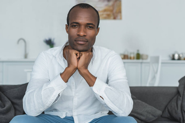handsome african american man resting chin on hands and looking at camera at home - Photo, Image