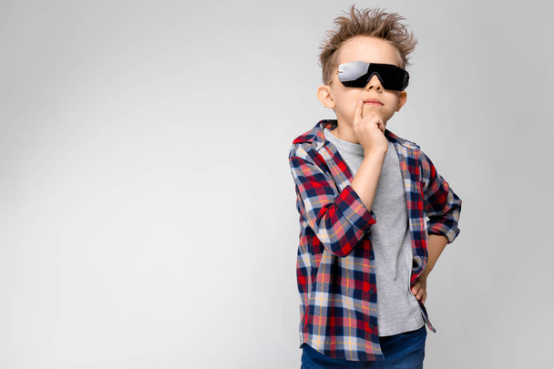 Niza niño preescolar caucásico en traje casual y gafas de sol que muestran diferentes expresiones en la pared blanca en el estudio
. - Foto, Imagen