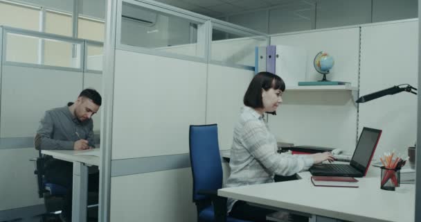 Εργάσιμη ημέρα στο γραφείο, νέοι επανδρώνει και γυναίκα κάθεται στο τους επιφάνεια εργασίας συμπύκνωμα, νεαρή γυναίκα να λάβει μια συνομιλία με τον συνάδελφό της ζητώντας κάτι. 4k - Πλάνα, βίντεο