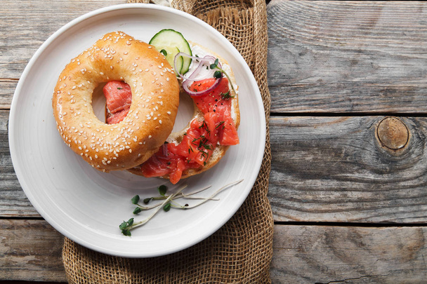 bagel with salmon fish and cream cheese with cucumber and fresh radish slices on white plate  - Φωτογραφία, εικόνα