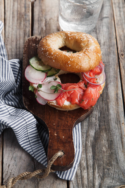 bagel with salmon fish and cream cheese with cucumber and fresh radish slices  on wooden cutting board, close-up  - Foto, Bild