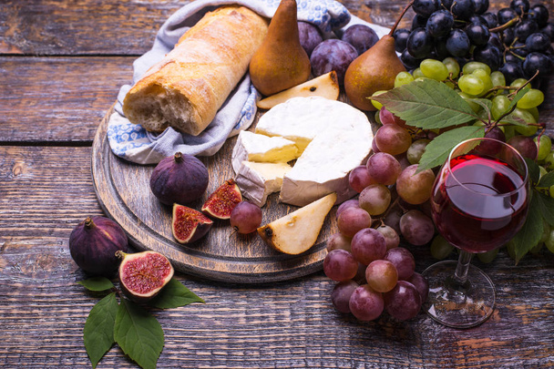 Red wine in a glass, cork, bottle screw and a set of products - cheese, grapes, nuts, olives, figs, pears, bread, autumn foliage  on a wooden board, background - Foto, Bild
