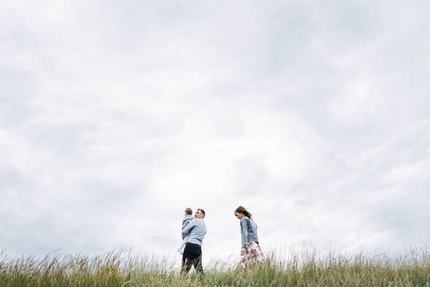 Vista inferior de la familia caminando en el prado contra el fondo nublado del cielo
 - Foto, Imagen