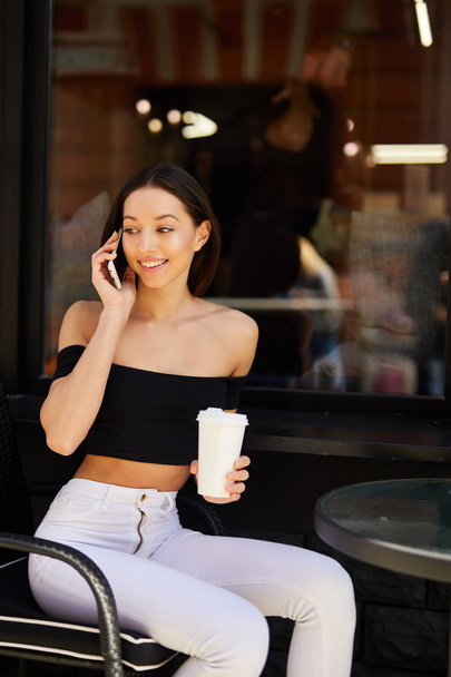 Pretty girl sit near coffee place and talk at her phone - Φωτογραφία, εικόνα