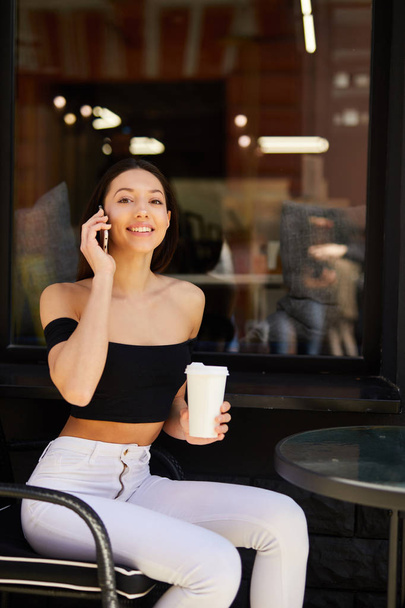 Pretty girl sit near coffee place and talk at her phone - Фото, зображення