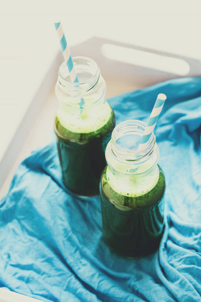 Healthy green smoothie made from spinach, apple and cucumber in a jars with red straw on white wooden table. Toned - Foto, immagini