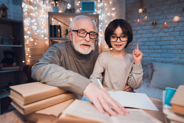 Grandfather helping grandson doing homework at table - Foto, immagini